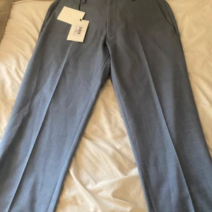 Ljusblå kostymbyxor Tiger of Sweden - Snygga ljusblå kostymbyxor från Tiger of Sweden i klassisk rak modell. Byxorna har pressveck, sidfickor och bälteshällor. Perfekta för en stilren look och tillverkade i ett tunt, elegant tyg som känns exklusivt.