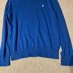 Blå stickad tröja från Polo Ralph Lauren, jr L men passar XS - Storken L 14-16 men passar XS. Klassisk blå stickad tröja från Polo Ralph Lauren med rund halsringning och broderad vit logga på bröstet. Tröjan har ribbade muddar vid ärmslut och nederkant, perfekt för en stilren och enkel look. Knappt använd och är i väldigt fint skick. Pris kan diskuteras, skriv vid funderingar