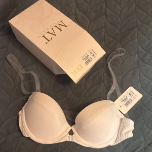 Vit bh från MAT Paula - Supersnygg vit bh från MAT, modell Paula. Den har släta kupor med lätt vaddering och transparenta axelband som ger en clean look. Kuporna är formade för bra stöd.