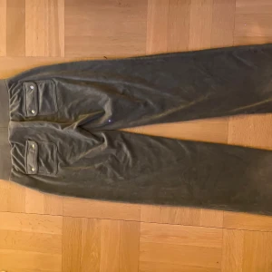 Gröna juicy mjukis - Snygga gröna juicy mjukis med bred resår och snörning i midjan. Byxorna har raka ben och två stora fickor med lock och knappar bak. Perfekta för en chill och avslappnad stil.