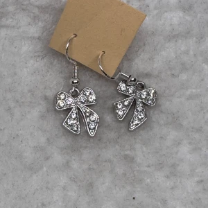 Glittriga örhängen med rosettform - Supersöta örhängen i silverfärg med gnistrande stenar och rosettform. Perfekta för dig som vill ha en söt och glittrig detalj till din look. Hängande modell som ger extra bling till outfiten. Krokarna är i sterling silver 