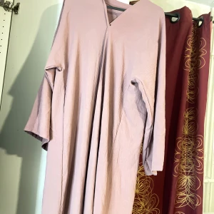 Ljusrosa öppen abaya  med v-ringning - En flowy öppen abaya ljuslrosa med v-ringad hals och vida, långa ärmar. Klänningen har en enkel och minimalistisk design utan mönster eller detaljer, perfekt för dig som gillar en chill och avslappnad stil.
