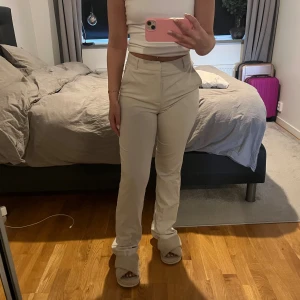 Beiga kostymbyxor - Snygga beiga kostymbyxor med hög midja och lite vida ben. Byxorna har klassisk passform med hällor för bälte och stängs med dragkedja och knapp. Perfekta för en clean och stilren look. Passar både 34 & 36 då det är stretchig material 