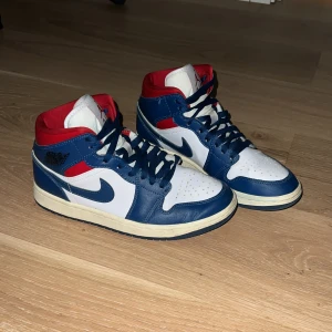 Nike Air Jordan 1 Mid blå/röd/vit - Nike Air Jordan 1 Mid sneakers i blått, vitt och rött. Perfekt för dig som gillar streetwear! Nypris 1999 kr och nästan helt oanvända. Skick 9,5/10! Priset är inte hugget i sten!