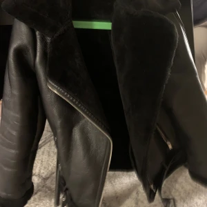 Svart teddyjacka i skinnimitation - Säljer en svart teddyjacka med stora slag och dragkedjor. Utsidan är i skinnimitation och insidan är fodrad med mjuk teddy. Jackan har en cool, oversized look och passar perfekt när du vill ha en edgy stil.