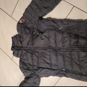 Svart dunjacka Parajumpers M - Säljer en svart dunjacka från Parajumpers i storlek M. Jackan är superlätt, har quiltad design, dragkedja framtill och flera fickor. Insidan är ljusbeige och jackan har en patch på ena ärmen. Perfekt för kalla dagar när du vill hålla stilen. Tyvärr har ena innerfickan lossnat lite men ingen man märket eller som syns.