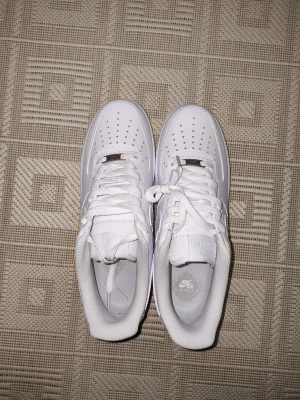 NAF 1 vita sneakers - NAF 1 sneakers i helvitt med klassisk låg siluett. Skorna har perforerad tå, snörning och platt sula. Tillverkade i skinn med mjukt foder och tydlig N-logga på sidan och hälen. Perfekt för dig som gillar clean och stilren streetwear.