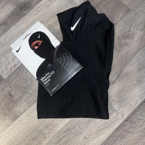 Nike Pro svart balaclava hood - Nike Pro Therma-FIT Hood i svart med vit logga. Balaclava-modell som täcker hela huvudet och halsen, perfekt för träning utomhus eller kyliga dagar. Tillverkad i mjukt och stretchigt syntetmaterial som andas och håller värmen. Kan sänka pris vid snabb affär och snabb frakt 