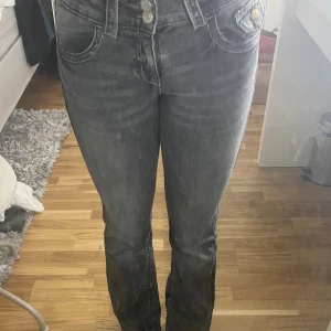 Grå bootcut jeans från Gina Tricot - Snygga grå jeans från Gina Tricot med bootcut passform och hög midja. Jeansen har tydliga vita sömmar, dubbla silverknappar och dragkedja i gylfen. Materialet är klassisk jeans med lätt tvättad look och fem fickor.