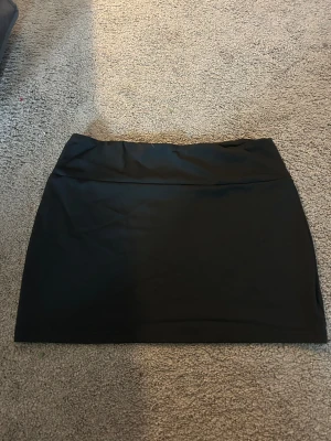 Svart kortkjol i polyester - En stilren svart kortkjol med enkel design och rak passform. Kjolen är tillverkad i mjukt polyester-material och har en slät yta utan mönster eller detaljer. Perfekt för dig som gillar minimalistisk stil och vill ha en klassisk bas i garderoben. OBS, low waist och kan vara väldigt kort beroende på kroppsform, kan användas som topp också❤️(har 2st)