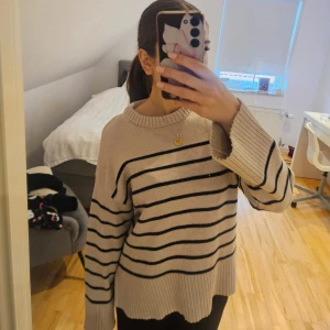 Beige randig stickad tröja - Säljer en beige stickad tröja med svarta horisontella ränder. Tröjan har en avslappnad passform, breda ribbade muddar och rund halsringning. Perfekt för lager-på-lager och chill dagar.