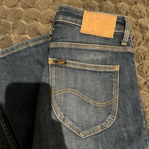 Lee Breese Boot jeans blå W27 L33 - Snygga Lee Breese Boot jeans i klassisk blå tvätt med kontrastsömmar och bootcut-ben. Modellen har 4 fickor, normal passform och är tillverkad i mjukt jeanstyg. Perfekt för dig som gillar en tidlös look med lite extra vidd vid benslutet.