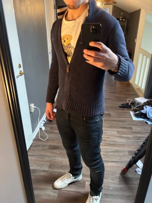 Marinblå kofta från Ralph Lauren - Säljer en marinblå stickad kofta från Ralph Lauren med dragkedja och ribbade muddar. Koftan har en ståkrage med randig insida och den klassiska broderade loggan på bröstet. Perfekt för lager-på-lager och snygg till jeans. Det är i barnstorlek men sitter som S.