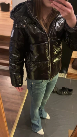 Svart pufferjacka från Nelly XS - Säljer en svart, glansig pufferjacka från Nelly i storlek XS. Jackan har huva, dragkedja framtill och är quiltad med en riktigt snygg oversized look. Perfekt för kalla dagar när du vill vara både varm och stilren.den saknar en knapp vid jackfickan men annars fint skick. Original priset är runt 700 kr. 