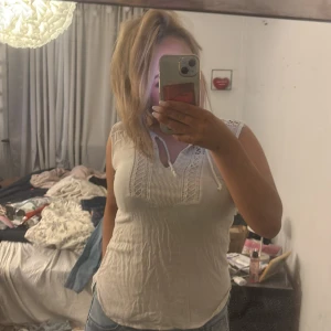 Vit ärmlös linnetopp med spets - Säljer en vit ärmlös linnetopp med snygga spetsdetaljer och knyt vid halsen. Toppen har en lätt ribbad struktur framtill och är figurnära med rundad nederkant. Perfekt för dig som gillar en enkel men ändå söt look.