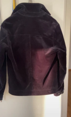 Svart manchesterjacka från Riley - Säljer en svart manchesterjacka från Riley med ståkrage och hel dragkedja framtill. Jackan har två fickor med dragkedja och snygga tryckknappar vid ärmsluten. Insidan är fodrad i blått tyg. Perfekt för dig som gillar stilrena och klassiska plagg.