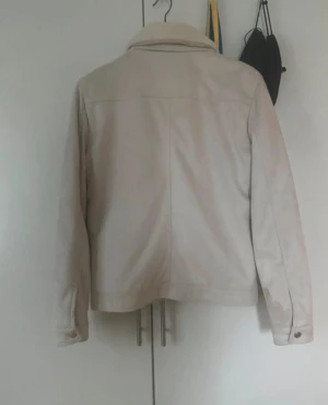 Beige teddyjacka från Zara - Snygg beige teddyjacka från Zara med mjuk krage i pälsimitation och quiltat foder. Jackan har två bröstfickor med knappar, sidofickor och stängs med både dragkedja och knappar. Perfekt för dig som gillar stilren och cozy look.