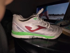 Vita Joma fotbollsskor med gröna detaljer - Säljer ett par vita Joma regate rebound  med gröna och röda detaljer. Skorna har snörning, platt sula med hexagonmönster och är tillverkade i syntetmaterial. Snyggt röd Joma-logga på sidan och grönt parti vid sulan. Perfekta för dig som vill sticka ut på planen använda 6 gånger men i gott skick det är stl 40 men för de som inte vet så är joma skor i stl för stora så stl 40 motsvarar stl 41 i nike eller adidas.