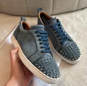 Washed blue Christian Louboutin - Säljer ett par blå sneakers från Christian Louboutin i mocka med coola nitar på tån. Skorna har blå snörning, vit sula och en snygg, rund tå. Perfekta för dig som vill sticka ut med en edgy vibe. Ändast dustbags skickas med samt en nit saknas där av pris. Storlek 44 hör av er vid frågor!