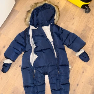 Murmelbear blå overall, storlek 18 mån + - Vinteroverall i blått med luva och fuskpäls. Overallen har dragkedja framtill och muddar vid ärmar och fötter. Perfekt för kyliga tider för att hålla 👶🏻 varm om vintern 🎁 nypris 499