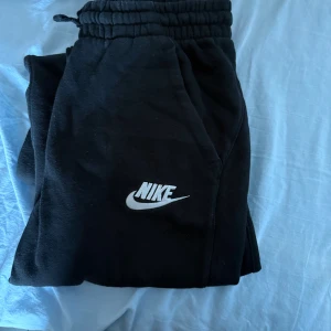 Svarta mjukisbyxor från Nike XL - Svarta mjukisbyxor från Nike i storlek XL med klassisk vit Nike-logga på benet. Byxorna har resår och snörning i midjan för skön passform och är gjorda i mjukt bomullsmaterial. Perfekta för chill eller träning.