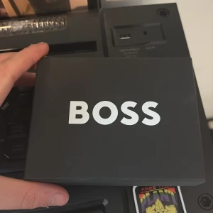 Svart plånbok från BOSS i skinn - Snygg svart plånbok från BOSS i äkta skinn med stilren design. Plånboken har flera kortfack, sedelfack och en praktisk myntficka. Perfekt storlek för att ha med sig överallt och BOSS-logga i silver på framsidan. Helt ny, köpte fel