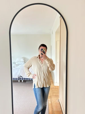 Beige ribbad skjorta från Abercrombie and Fitch - Beige skjorta från Abercrombie and Fitch i ribbad, mjuk polyester. Långärmad med klassisk krage och knappar framtill. Skjortan har en loose fit och diskreta slitsar i sidorna. Perfekt för en chill och avslappnad look.