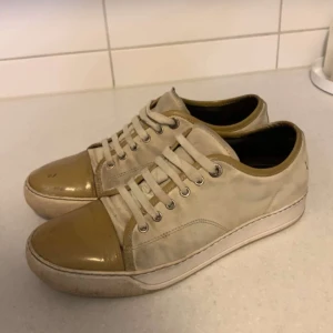 Beige sneakers med guldig tå - Snygga sneakers i beige canvas med guldig, glansig tå och matchande detaljer. Skorna har vita snören, rund tå och vit sula. Perfekta för dig som gillar en stilren men ändå unik look. Passar till det mesta och ger en cool touch till outfiten.