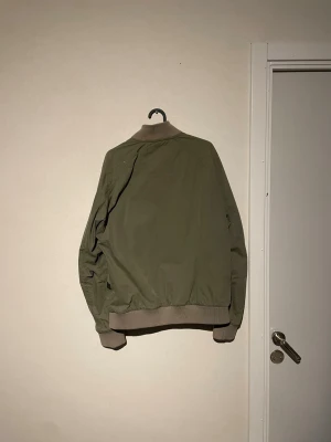 Olivgrön bomberjacka från G-Star RAW - Snygg olivgrön bomberjacka från G-Star RAW med ribbade muddar och krage i beige. Jackan har dragkedja framtill, två snedställda fickor och en ärmficka. Perfekt för dig som gillar en clean och stilren look.