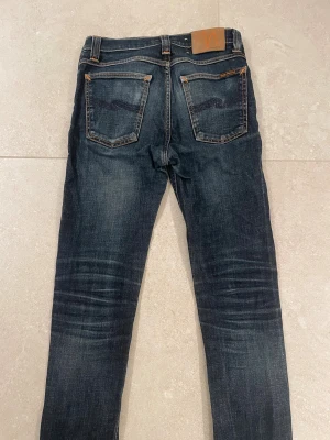 Nudie jeans med sköna slitningar! - Snygga mörkblå jeans från Nudie Jeans med slim passform. Modellen har fem fickor, låg midja och raka ben med slitningar för en cool look. Perfekt för dig som gillar en smal siluett och streetstyle.
