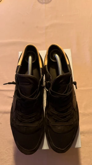 Svarta sneakers från Philippe Model - Säljer ett par svarta sneakers från Philippe Model med snygga detaljer i skinn och mocka. Skorna har snörning, rund tå och en beige kant på sulan som ger en cool kontrast. Perfekta för dig som gillar stilrena och trendiga sneakers.