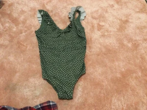 Grön prickig baddräkt från H&M - Supersöt grön baddräkt från H&M med vita prickar och volangdetaljer på axelbanden. Djup v-ringning både fram och bak. Perfekt för strand eller poolhäng i sommar! Tillverkad i mjukt och stretchigt material som sitter skönt.