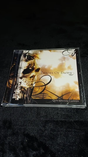 Throes Of Dawn - Quicksilver Clouds (Enhanced CD) - Snyggt exemplar av Throes Of Dawn-albumet 'Quicksilver Clouds' på Enhanced CD. Fodral och skiva i mycket gott skick, med original artwork och låtlista. Innehåller bonusvideo 'Vertigo'. Perfekt för samlare och fans av bandet.