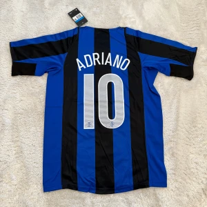 Inter Milan Adriano #10 fotbollströja - Säljer en klassisk Inter Milan fotbollströja från Nike med Adriano och nummer 10 på ryggen. Tröjan har blå och svarta vertikala ränder, korta ärmar och Pirelli-logga på bröstet. Materialet är lätt och andas, perfekt för match eller träning.