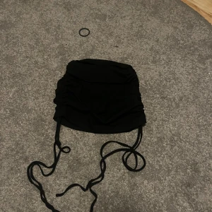 Svart kortkjol med snörning -  svart kortkjol med  snörning på sidorna och rynkade detaljer. Kjolen är i ett stretchigt, ribbat material som sitter tight. Den är från SHEIN och storlek S 