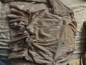 Champagnefärgad omlottblus Gina Tricot - Säljer en champagnefärgad omlottblus från Gina Tricot i storlek S. Blusen har glittrigt ribbat tyg, volangdetaljer och knyt i midjan. Perfekt för dig som gillar trendiga och festliga toppar med snygg passform och coola detaljer.