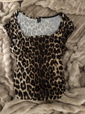 Leopardmönstrad topp från SHEIN - Säljer en snygg leopardmönstrad topp från SHEIN i storlek S. Toppen har rundad halsringning och korta ärmar. Materialet är mjukt och stretchigt polyester, perfekt för dig som gillar djurmönster och vill sticka ut med din stil.