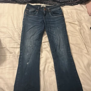 Blå jeans från LTB med raka ben - Snygga blå jeans från LTB med klassisk femficksdesign och raka ben. Jeansen har slitningar och diskreta detaljer på både fram- och baksida, samt kontrastsömmar och knappstängning. Perfekt för dig som gillar en avslappnad och tidlös look.
