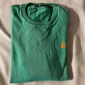 SailRacing Grön stickad tröja - Grön stickad tröja från Sail Racing i storlek XS. Rund hals med ribbade muddar och långärmad design. Tröjan har en orange broderad logga på bröstet som ger en snygg detalj. Perfekt för dig som gillar stilrena och sportiga plagg. Först till kvarn! 