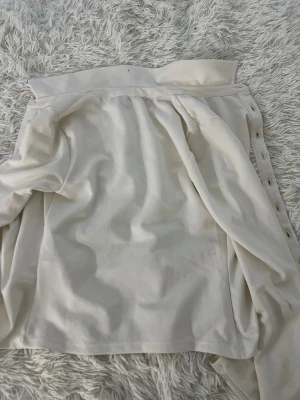 Vit skjorta med rynkade detaljer BikBok - Snygg vit skjorta från BikBok i storlek XS. Skjortan har långa ärmar, klassisk krage och knappar framtill. Materialet är mjukt och har en lätt glans. Rynkade detaljer längs knappraden ger en cool och modern look.