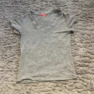 Grå v-ringad topp från RYVLS - Grå v-ringad topp från Stryls i mjuk bomull. Kortärmad och med en slim passform som sitter snyggt på kroppen. Perfekt att matcha med jeans eller kjol för en enkel och clean look.