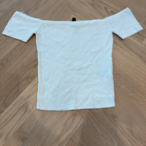 Vit offshoulder topp från H&M Divided - Säljer en vit offshoulder topp från H&M Divided i storlek S. Toppen är ribbad och har korta ärmar som sitter snyggt över axlarna. Materialet är mjukt och stretchigt, perfekt för en chill och stilren look. Passformen är tight och figurnära.