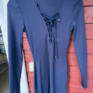Marinblå ribbad klänning Gina Tricot - Snygg marinblå ribbad klänning från Gina Tricot i storlek S. Klänningen har lång ärm, v-ringning med snörning framtill och är figurnära i modellen. Perfekt för dig som gillar stilrena detaljer och en enkel men cool look.