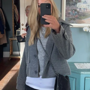 Grå kort kappa med stora knappar - Säljer en snygg grå kort rock med bred krage och stora knappar framtill. Jackan har lång ärm och två fickor fram.