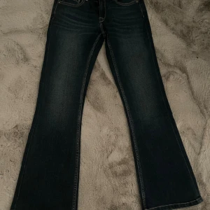 Bootcut jeans från Pepe Jeans - Mörkblå lågmidjade bootcut jeans från Pepe Jeans med klassisk femficksdesign och kontrastsömmar. Baktill finns två fickor med broderad detalj och ett brunt läderpatch med logga i midjan. Jeansen har en snygg tvätt och är tillverkade i jeansmaterial.