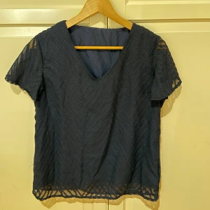 Mörkblå blus - Snygg mörkblå blus med korta ärmar och v-ringad hals. Blusen har ett transparent mönster i zigzag och är fodrad på kroppen men har genomskinliga ärmar. 
