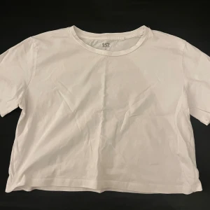 Vit t-shirt från lager157 - En enkel och fräsch vit mag t-shirt från lager 157 i storlek M. Modellen är rak med rund hals och korta ärmar. Tillverkad i 100% bomull för en mjuk och skön känsla. Perfekt för dig som gillar minimalistisk stil och vill ha en basic tee i garderoben. Använd en gång. 