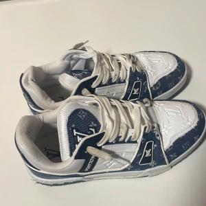 Louis Vuitton blåvita sneakers - Säljer ett par Louis Vuitton sneakers i blått och vitt med klassiskt LV-monogram över hela skon. Modellen har snörning, platt sula och rund tå. Materialet är en mix av skinn och textil, med tydliga LV-detaljer på både sidor och häl. Perfekt för dig som vill sticka ut med lyxig streetstyle. De är skitiga men sånt som går bort lätt. Blev lite snabba bilder då jag måste bli av med de fort. PRISET ÄR INTE HUGGET I STEN!