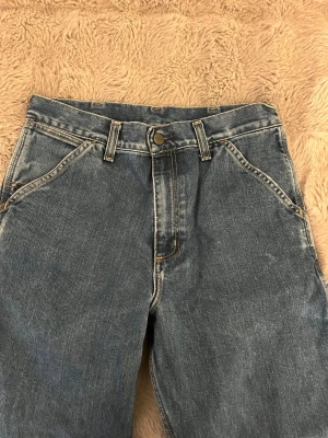 Carhartt blå cargopants i jeans - Säljer ett par blå cargopants från Carhartt med klassisk logga på bakfickan. Byxorna har raka ben, flera praktiska fickor och är gjorda i slitstarkt jeanstyg. 