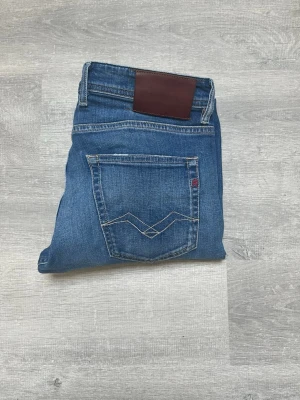 Replay Grover blå jeans straight fit - Säljer ett par Replay Grover jeans i klassisk blå tvätt. Modellen är straight fit med snygga kontrastsömmar och fem fickor. Jeansen har en mörkbrun patch bak i midjan och Replay-logga på fickan. Perfekta för dig som gillar en tidlös och clean look.